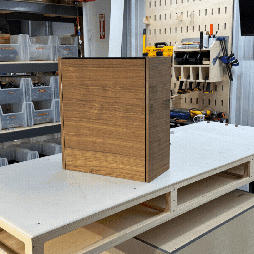 2_GIF A wooden cabinet box sits on a workbench in a workshop, with tools and storage bins visible in the background.