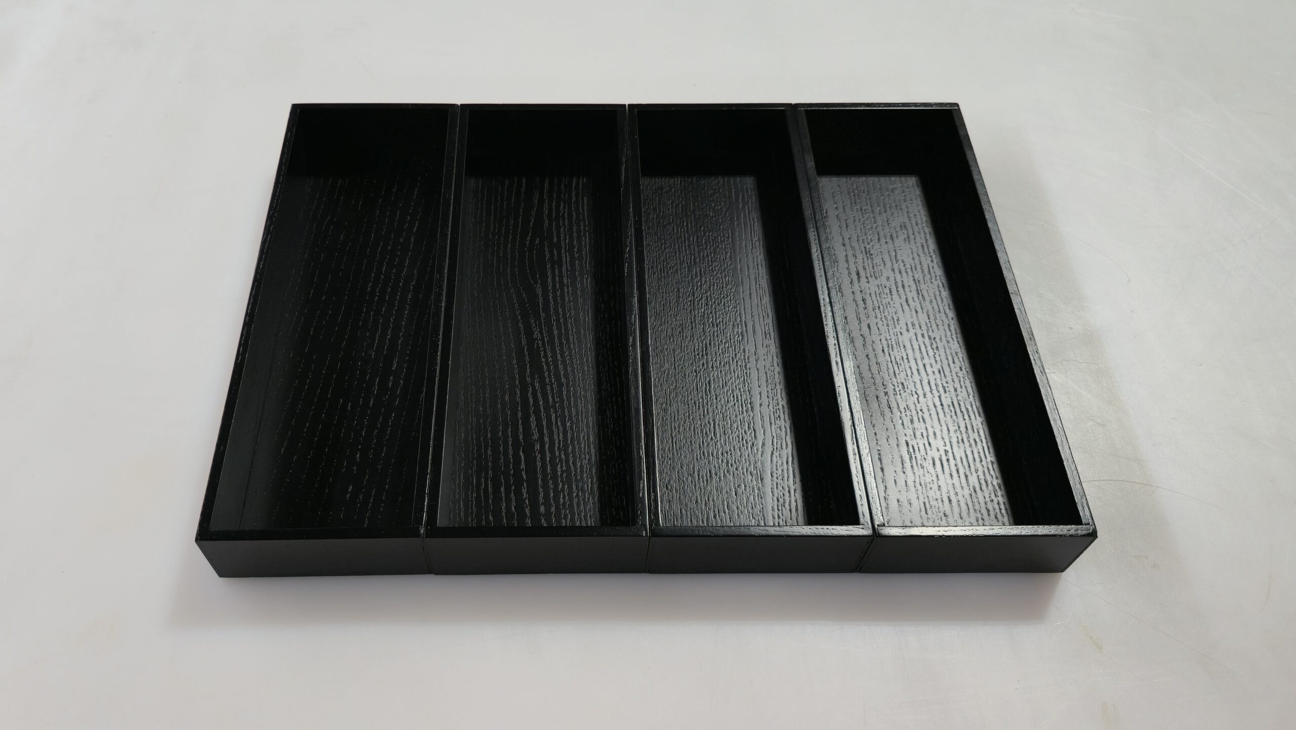 Espresso A Four empty, rectangular black wooden trays are arranged side by side on a white surface.