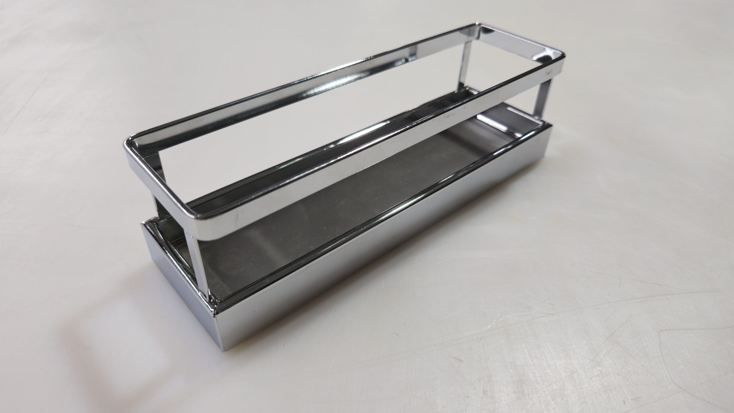 Espresso B A rectangular, chrome-finished metal shelf with open sides and a flat base, placed on a light-colored surface.