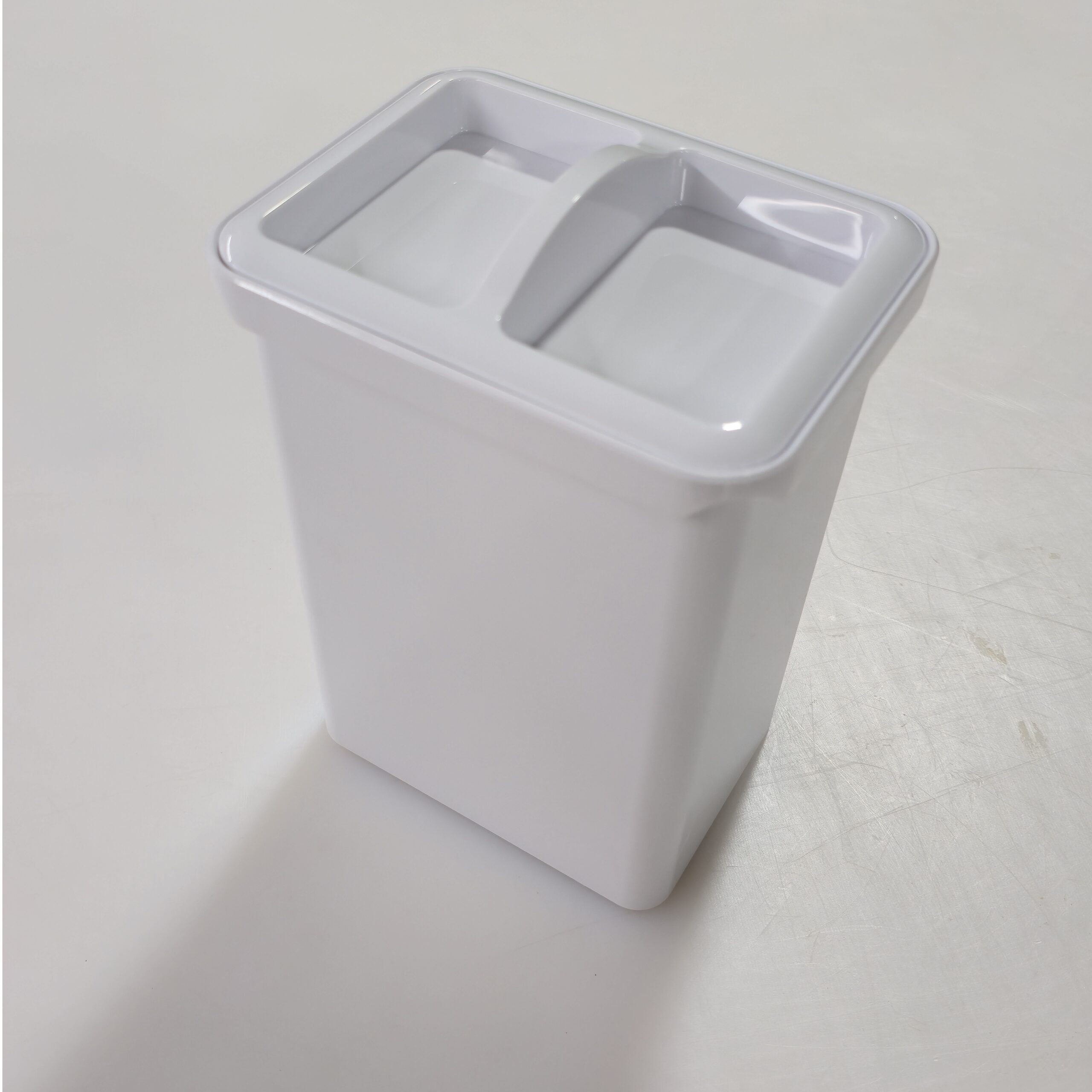 Espresso D A white rectangular plastic container with a divided lid sits on a plain, light-colored surface.